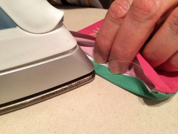 Holiday Coasters Tutorial - use the edge of your iron to fuse the edge of the folded fabric to the bottom edge of the insert