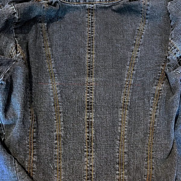 Remove the clips and press the jacket down to the sticky stabilizer. Placed correctly, when you unfold the jacket, the collar should be facing the top of the hoop. For a little more stability, you can pin the jacket to the stabilizer, but be careful to place your pins well away from the stitch areas (lay your printed design template over the marks on the jacket to clearly see the stitch area.)