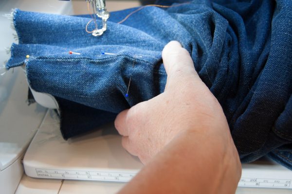 Waist first, slip the jeans over the free arm of the machine
