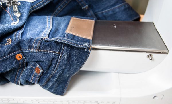 Waist first, slip the jeans over the free arm of the machin