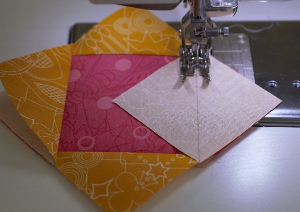 Place a square on each corner of the pink center square and sew on the diagonal line