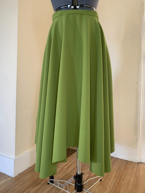 A green skirt on a mannequin with an uneven hem.