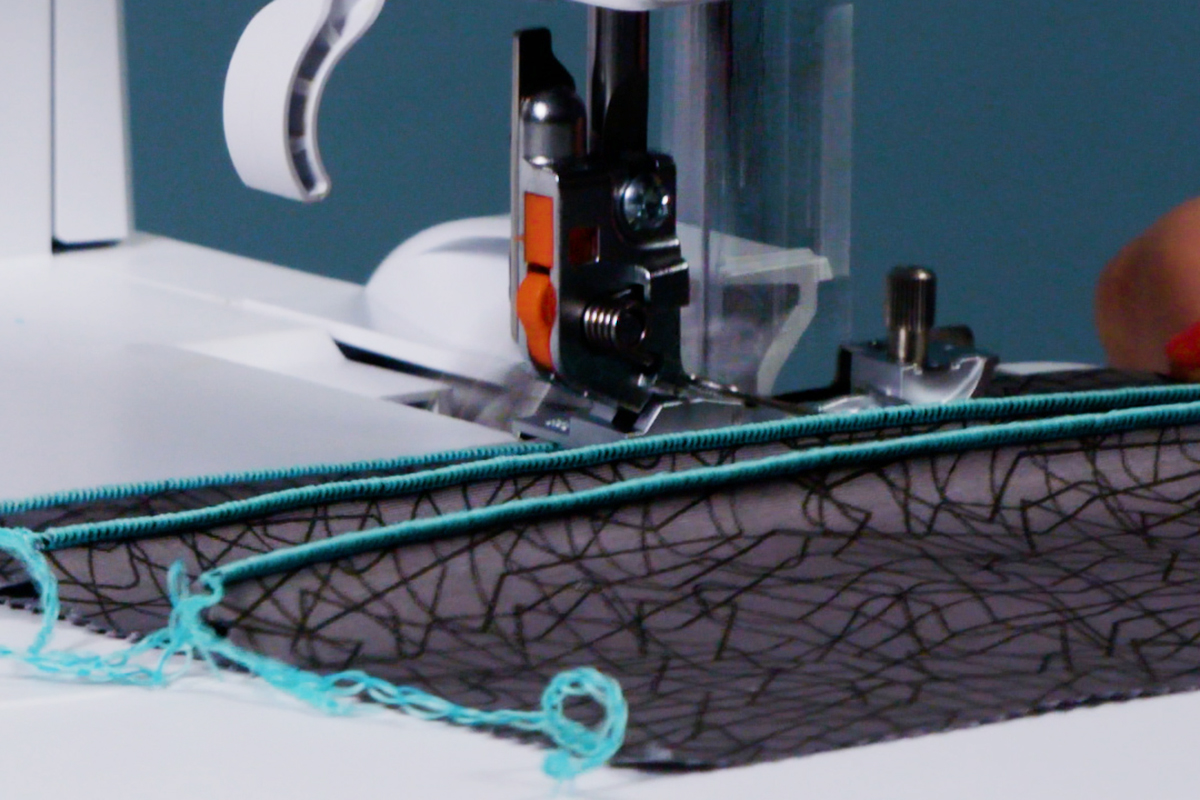 back view of black fabric being fed through a serger, highlighting the set up of multiple pintucks
