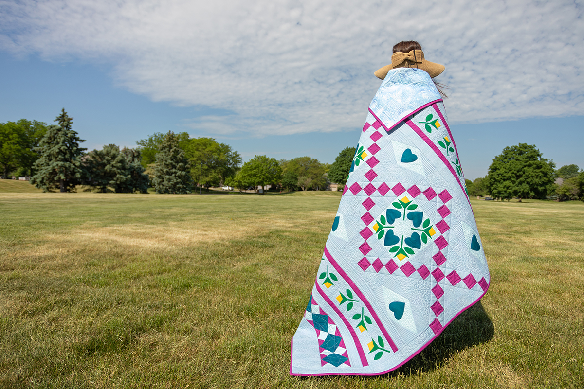 Jump for Joy quilt draped around a woman walking in a sunny field.