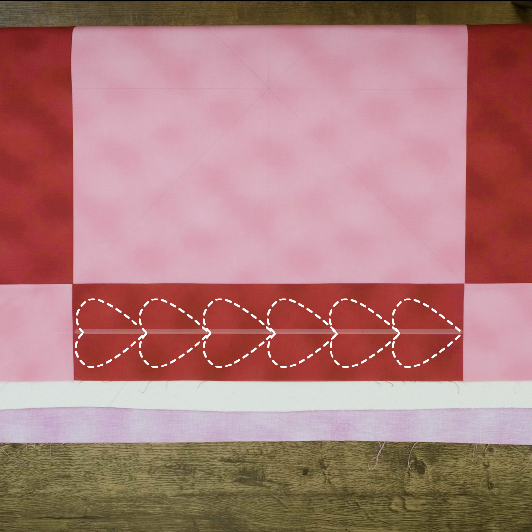 Overhead view of six hearts quilted onto the border of a red and pink checkered quilt