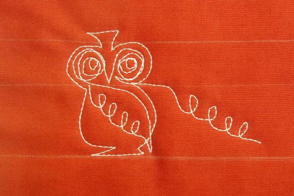 Close-up view of owl motif stitched onto orange fabric