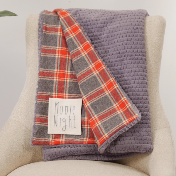 Plaid and purple throw blanket reading "movie night" draped over white chair