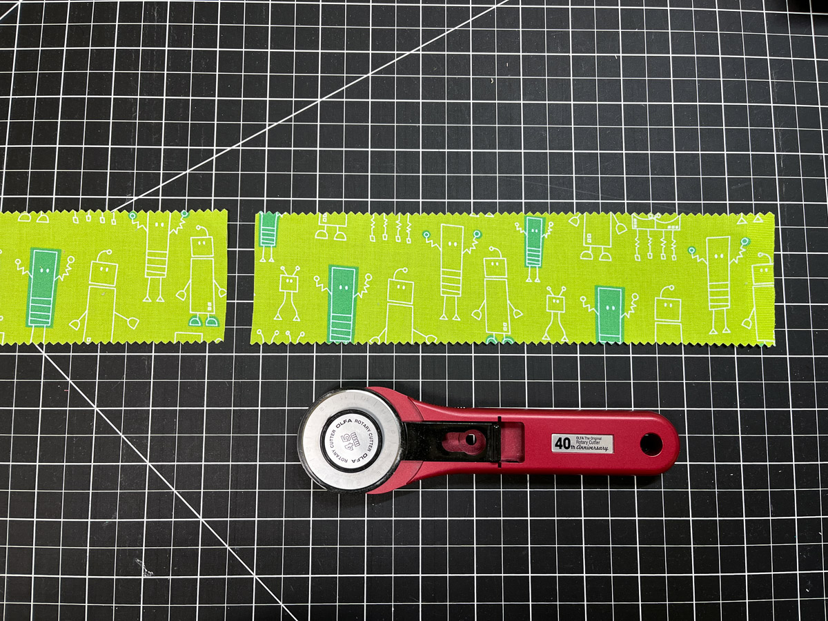 Green fabric strip and rotary knife on a black cutting board