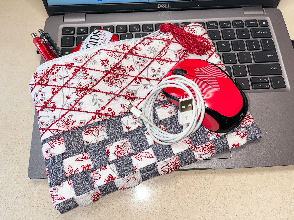 Woven zippered pouch arranged on laptop with pens, cord, and mouse