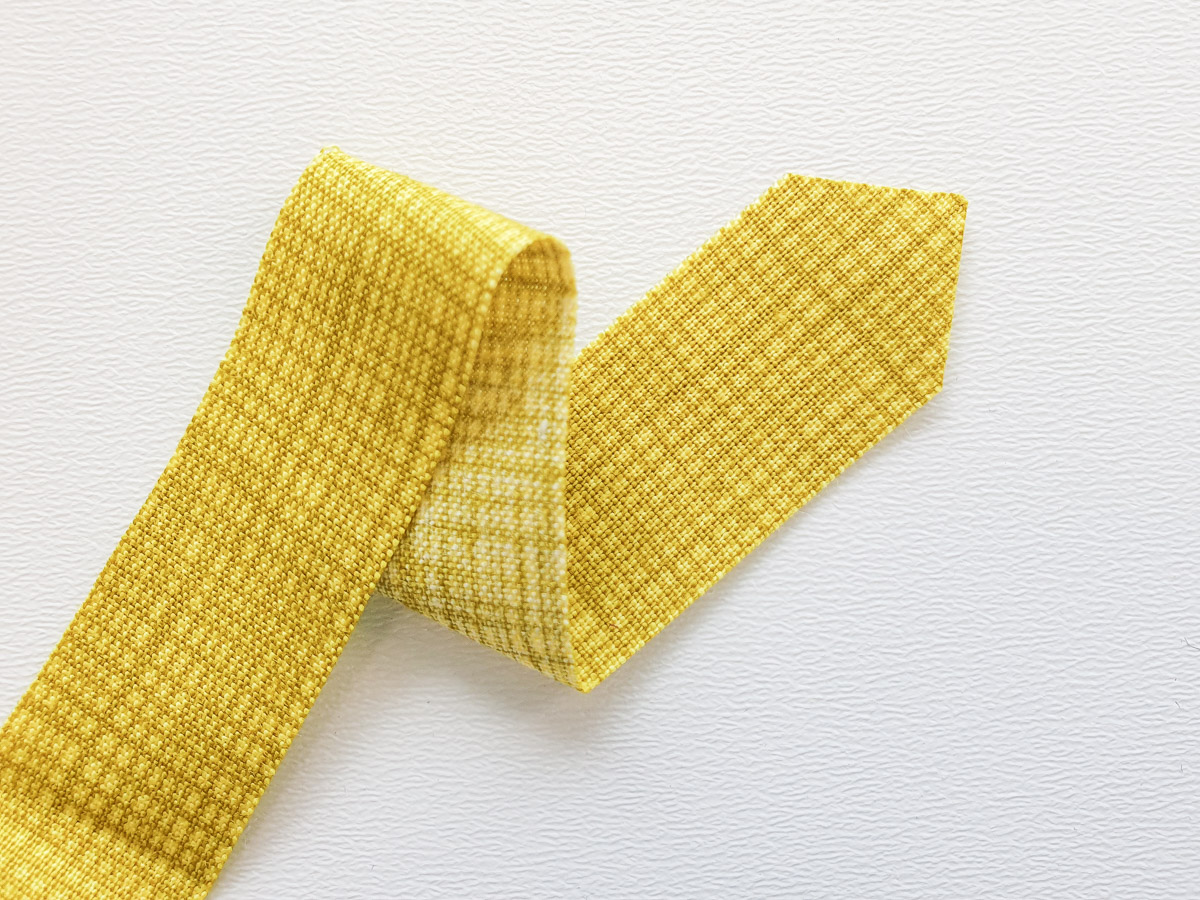 yellow strip of fabric with a pointed end on a white textured background