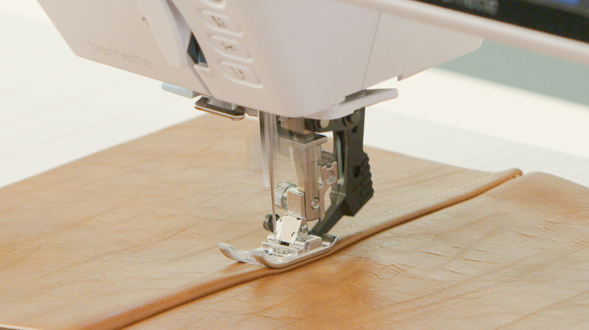 Close-up of sewing machine stitching brown leather fabric with precise seam