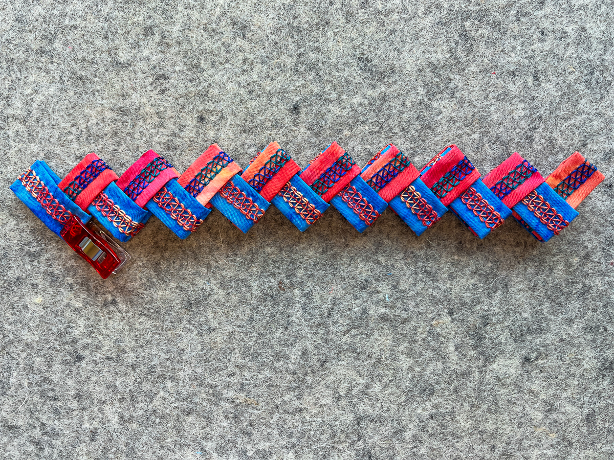 alternating colors of blue and orange folded pieces to form a bracelet on gray fabric