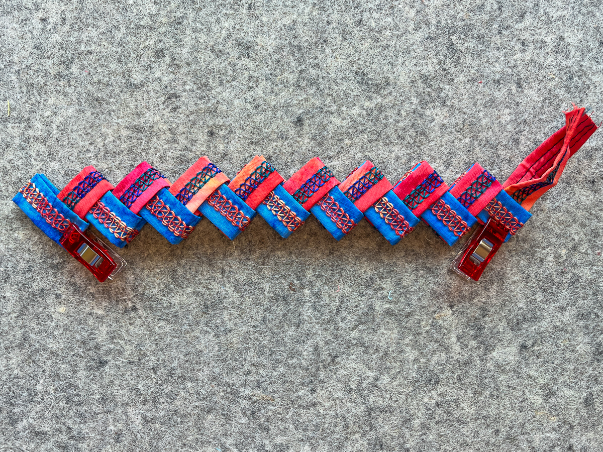 alternating colors of blue and orange folded pieces to form a serger cuff bracelet on gray fabric
