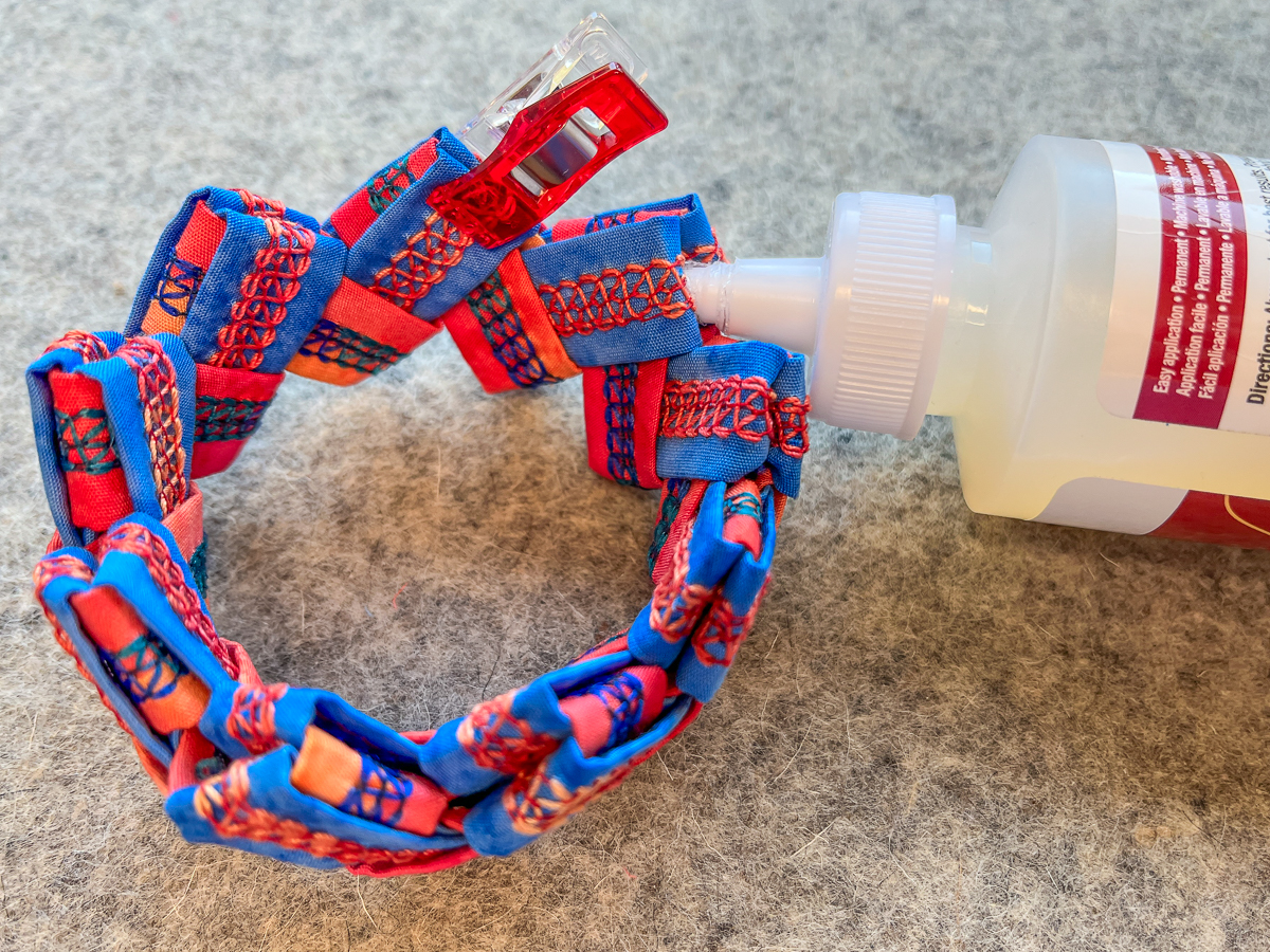 applying glue to the finished serger cuff bracelet in orange and blue fabric on a gray background