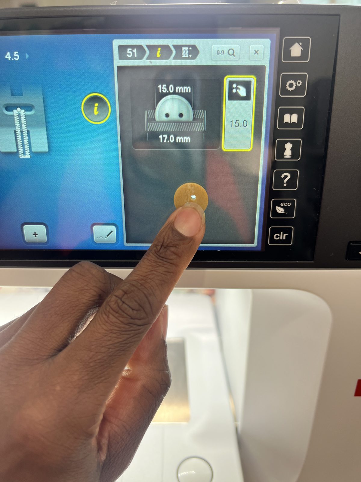 Hand holding a tan two-hole button against the BERNINA sewing machine touchscreen to match the buttonhole measurement, set to 15.0 mm