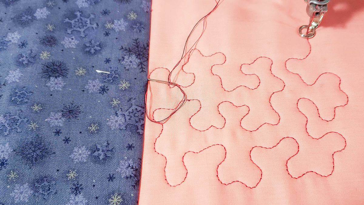 Overhead view of orange and blue/grey fabric, with quilted red thread.