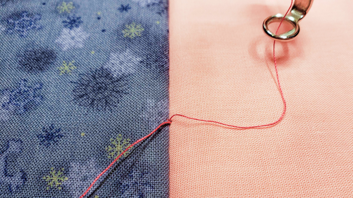 Overhead view of orange and blue/grey fabric, with quilted red thread.