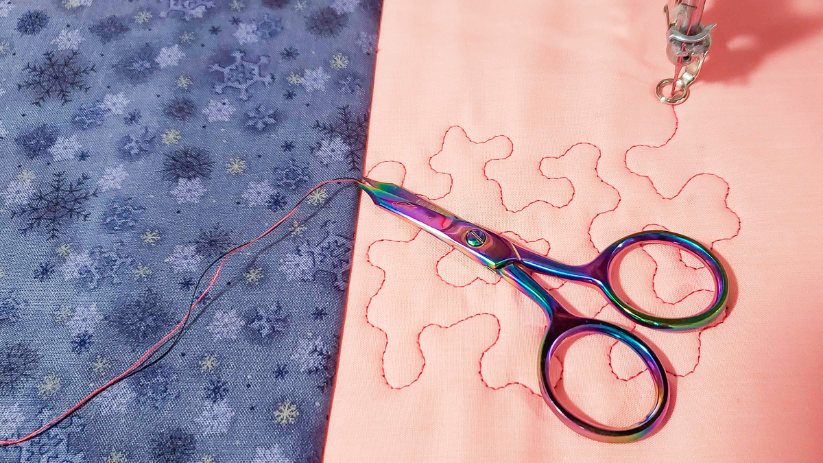 Overhead view of orange and blue/grey fabric, with quilted red thread and scissors.