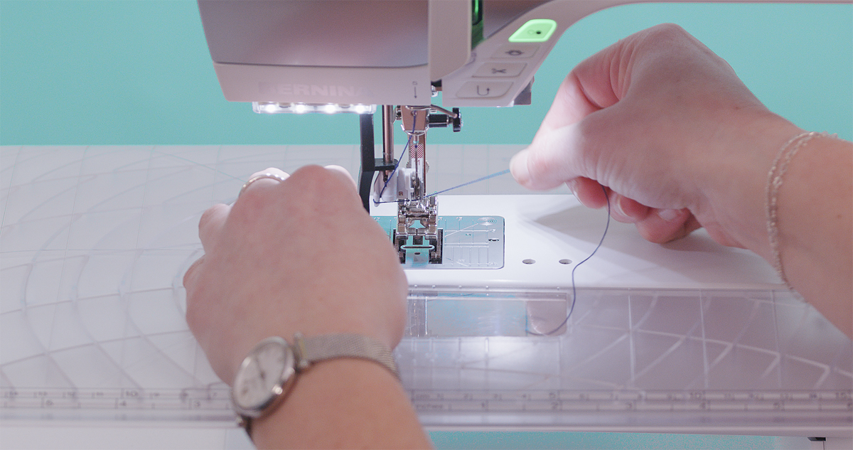 Close-up of hands threading a BERNINA sewing machine needle with the automatic needle threader