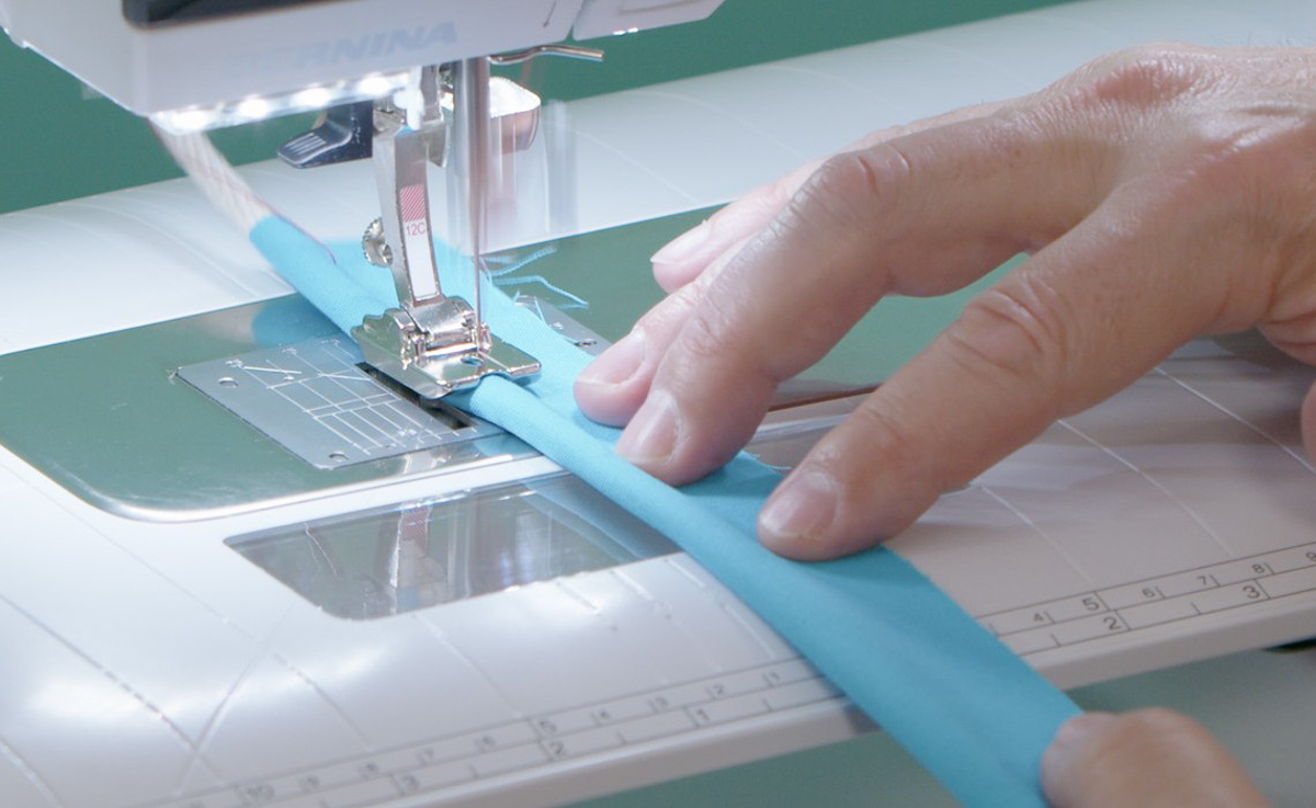 hands gently nudging blue fabric-wrapped cording through the sewing machine