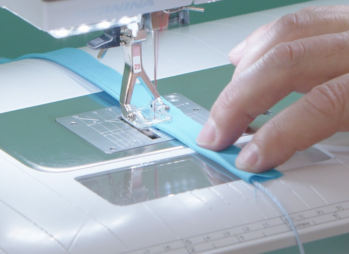hands gently nudging blue fabric-wrapped cording through the sewing machine