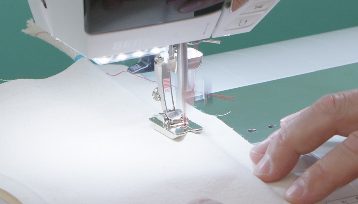 hands gently cream muslin fabric through the sewing machine